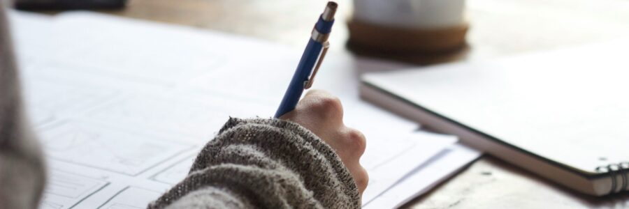 a person writing wearing a comfy gray sweater and there is a coffee nearby